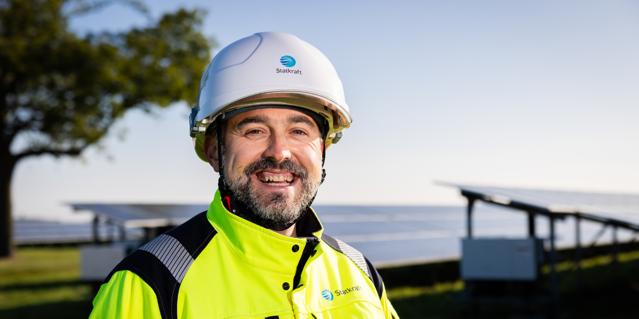 Uomo che indossa dispositivi di sicurezza sorridente con pannelli fotovoltaici sullo sfondo